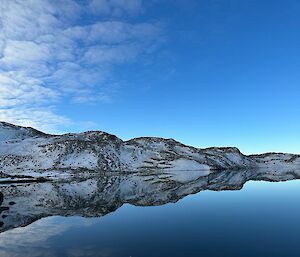 A mirrored lake reflecting back the snow-covered hills that surround it.