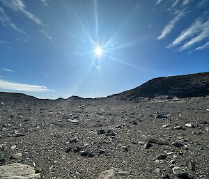 Looking across a rock covered landscape with the sun shining brightly overhead.