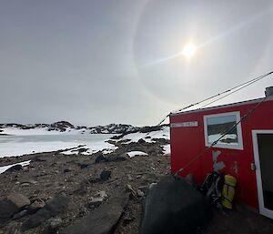 A red field hut set on a rocky outcrop surrounded by a snowy landscape