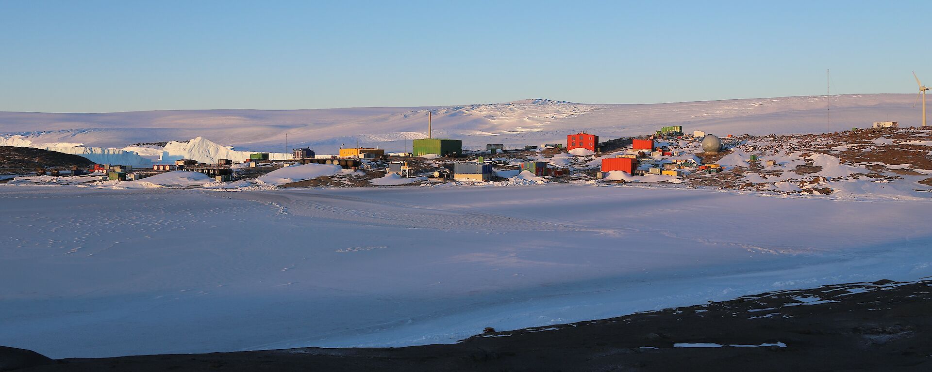 A station built upon a rocky landscape with ice covered harbour in the foreground and ice plateau rising in the distance