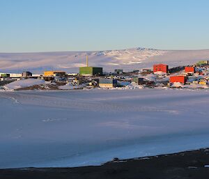 A station built upon a rocky landscape with ice covered harbour in the foreground and ice plateau rising in the distance