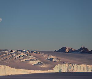 An icy landscape and rocky mountain range are in the distance beyond an ice covered sea