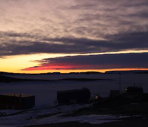 Twilight over an iced in sea with icebergs in the distance and red and orange tinted clouds