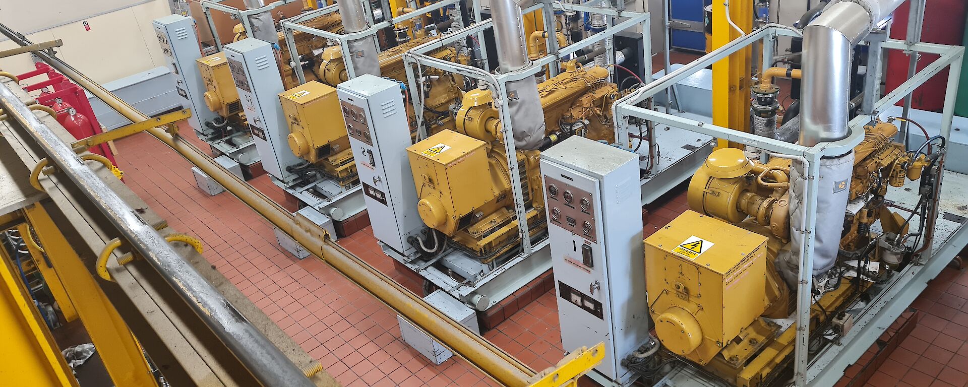 This photo is the inside of a machinery room. There are four identical yellow and grey generators that provide power to our station.