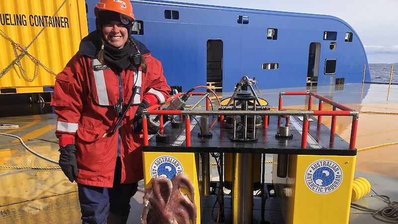 A woman in a red jacket stands next to a big yellow box used to spy on krill
