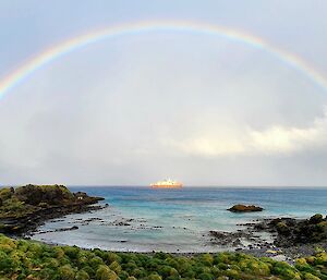 A large red and white ship sits offshore surrounded by a rainbow