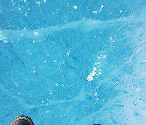 A pair of boots is in the bottom of the frame looking down into a frozen lake