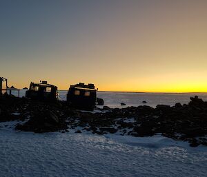 A Hägglunds vehicle is parked next to a hut with an ice plateau stretching into the sunset
