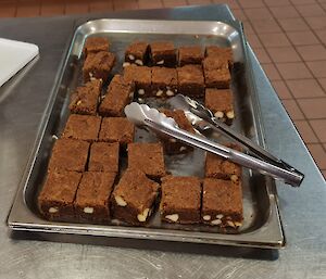 A tray of chocolate and macadamia nut brownies is on a bench