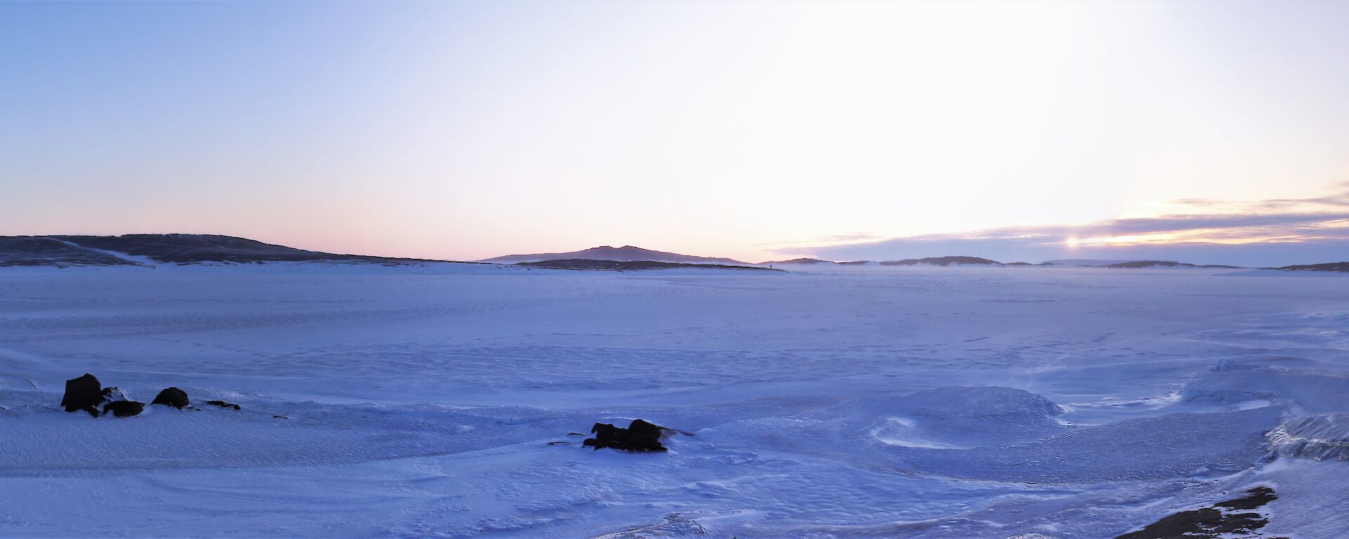 The sun is in the distance over a frozen harbour with a old hangar in the right of frame