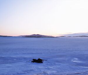 The sun is in the distance over a frozen harbour with a old hangar in the right of frame