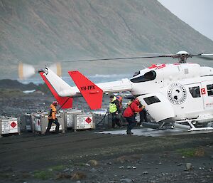 Helicopter operations being undertaken by people in hi vis on the grey shore of an island