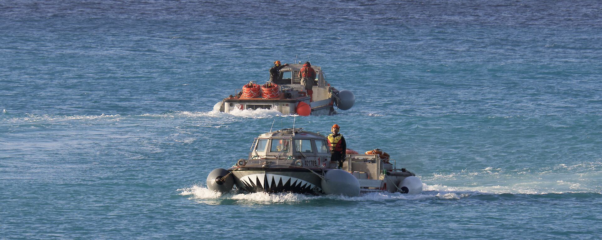 Two amphibious vehicles cross paths on the blue ocean