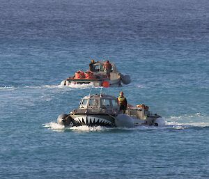 Two amphibious vehicles cross paths on the blue ocean