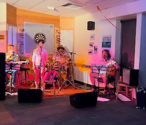 This photo is of the Casey band in action. From left to right there is a guitar player sitting, a lady standing at the microphone singing, the drummer in the background, and then another sitting guitar player. There is speaker equipment on the floor in front of the band.