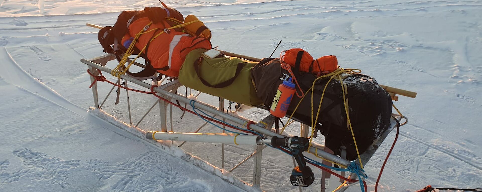 An aluminium sled carrying different coloured packs, sits on the sea-ice.