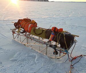 An aluminium sled carrying different coloured packs, sits on the sea-ice.
