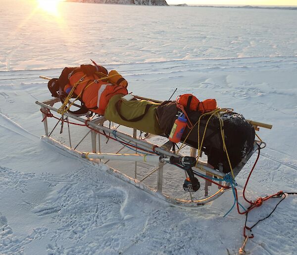 An aluminium sled carrying different coloured packs, sits on the sea-ice.