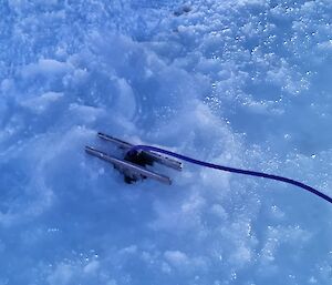 A metal wedge anchored into the sea-ice with a piece of string attacehd to it.