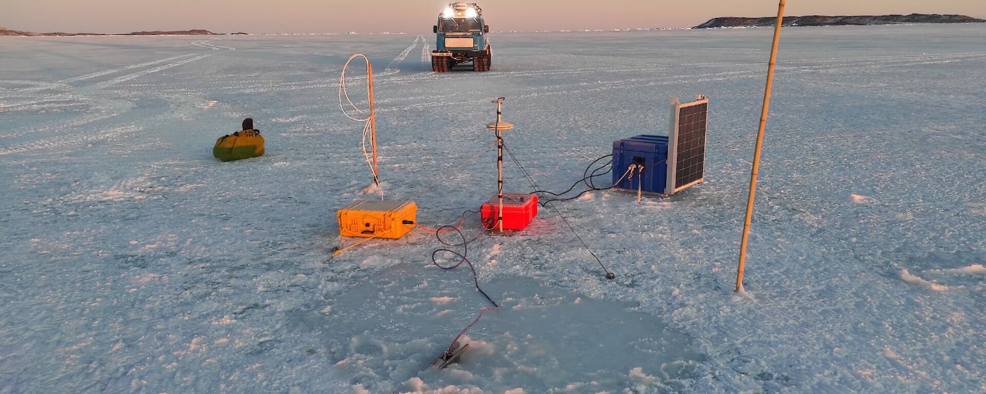 Sea-ice with scientific equipment on it with a Hagglunds (vehicle) in the background with its light on.
