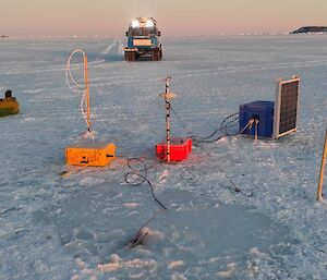 Sea-ice with scientific equipment on it with a Hagglunds (vehicle) in the background with its light on.