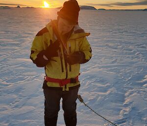 A man standing on the sea-ice uses his teeth to pull his tight thermal gloves off.