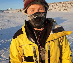 A man wearing a beanie and balaclava with icicles on his eyelashes and ice build-up around the edges of his beanie and on his balaclava.