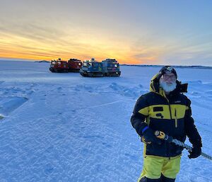 A man stands on the sea-ice holding a drill.