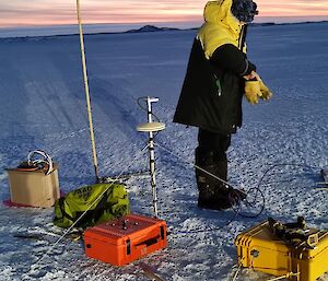 A man stands on the sea-ice next to colourful plastic suitcases filled with scientific equipment.