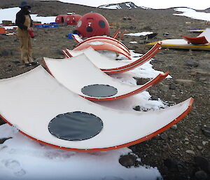 A person standing beside six triangular sections of a fibreglass hut laid out on rocky ground