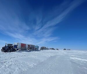 A series of tractors in a line pulling sleds laden with shipping containers