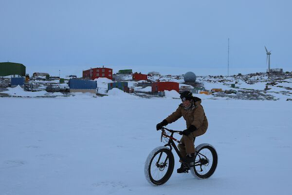 A man is riding a bicycle on the ice of a frozen harbour with station buildings in the background