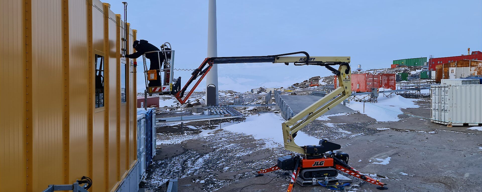 A man is on an elevated work platform repairing an antenna on the roof of a large yellow building