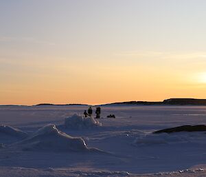A group of people are in the distance on an iced over harbour with the midday sun low on the horizon
