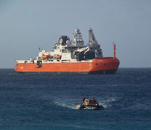 A small vessel heads to shore with a large red and white ship in the background