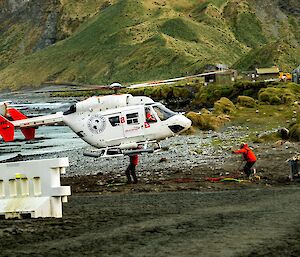 A white helicopter comes in to land on the grey shoreline of a green island