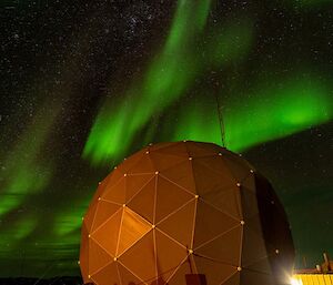 Swirling green lights in the night sky dance over a yellow dome shaped building.