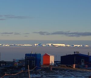 Station buildings in the foreground with the sea-ice in the mid-ground and icebergs on the horizon in the distance.