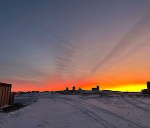 A red and yellow streaked sky as the sun rises causing silhouettes over station machinery and buildings.