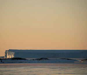 A tabular iceberg is lit by the setting sun in the distance