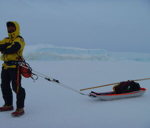 A man is standing on the sea-ice with arms crossed towing a sledge holding equipment