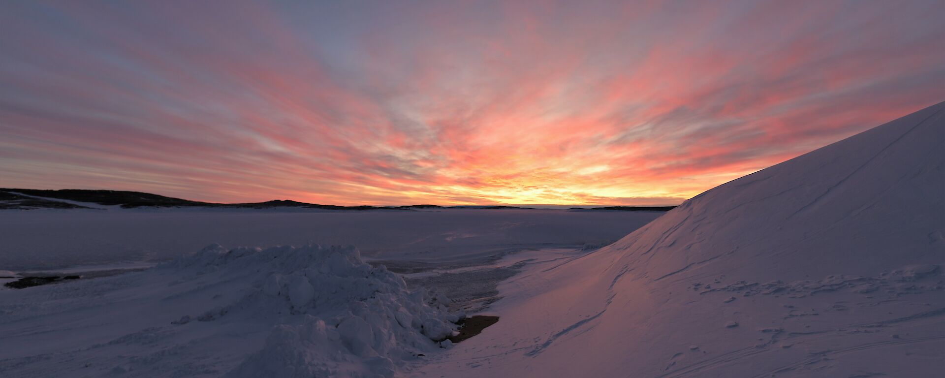 The sun is setting with clouds lit orange and red over the sea-ice