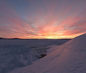 The sun is setting with clouds lit orange and red over the sea-ice