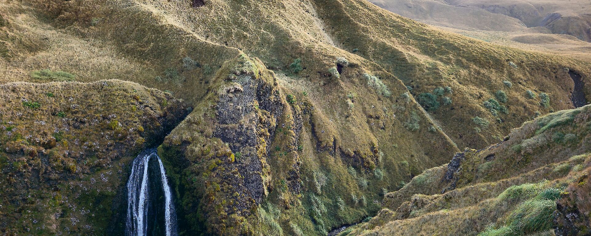 A waterfall is seen on a grassy green hil