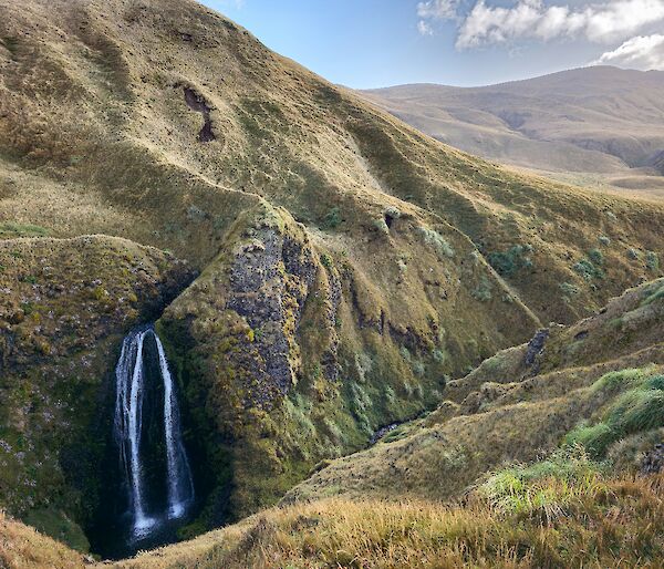 A waterfall is seen on a grassy green hil