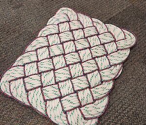 A woven white and red mat. The mat has been made from strands of white rope, with red rope providing the borders.