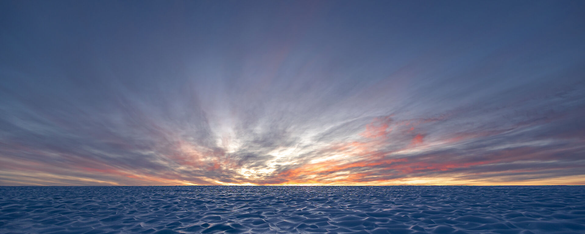 A brightly coloured sunset is in the distance over an vast field of ice
