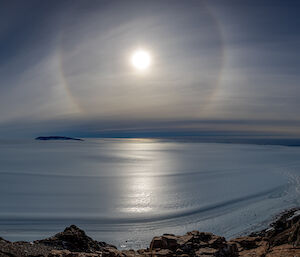 A vast ice plateau stretched into the distance with the sun surrounded by a halo in th sky above.