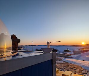 A bowl with noodles frozen solid as if being eaten with the spoon frozen into them sits on the edge of a blue insulated box. In the distance the sun is close to the horizon