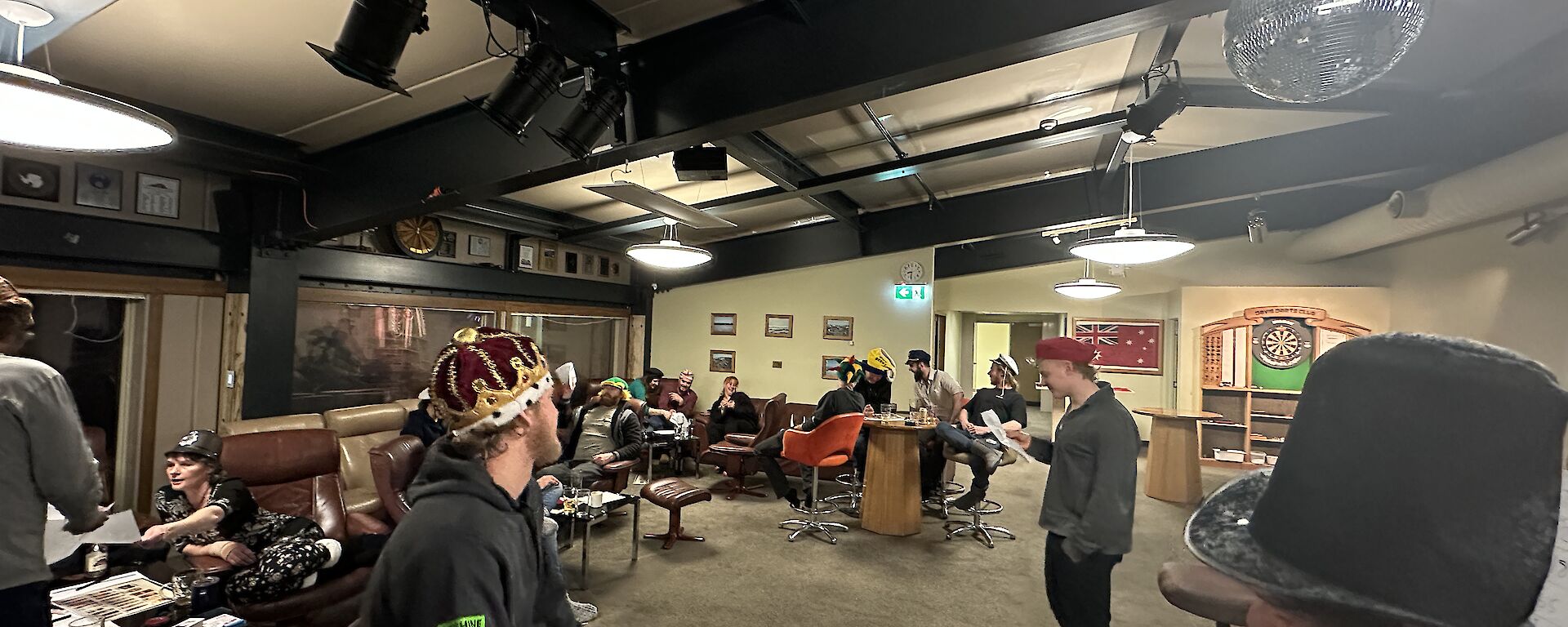 A group of people wearing costume hats seated around tables in a room.